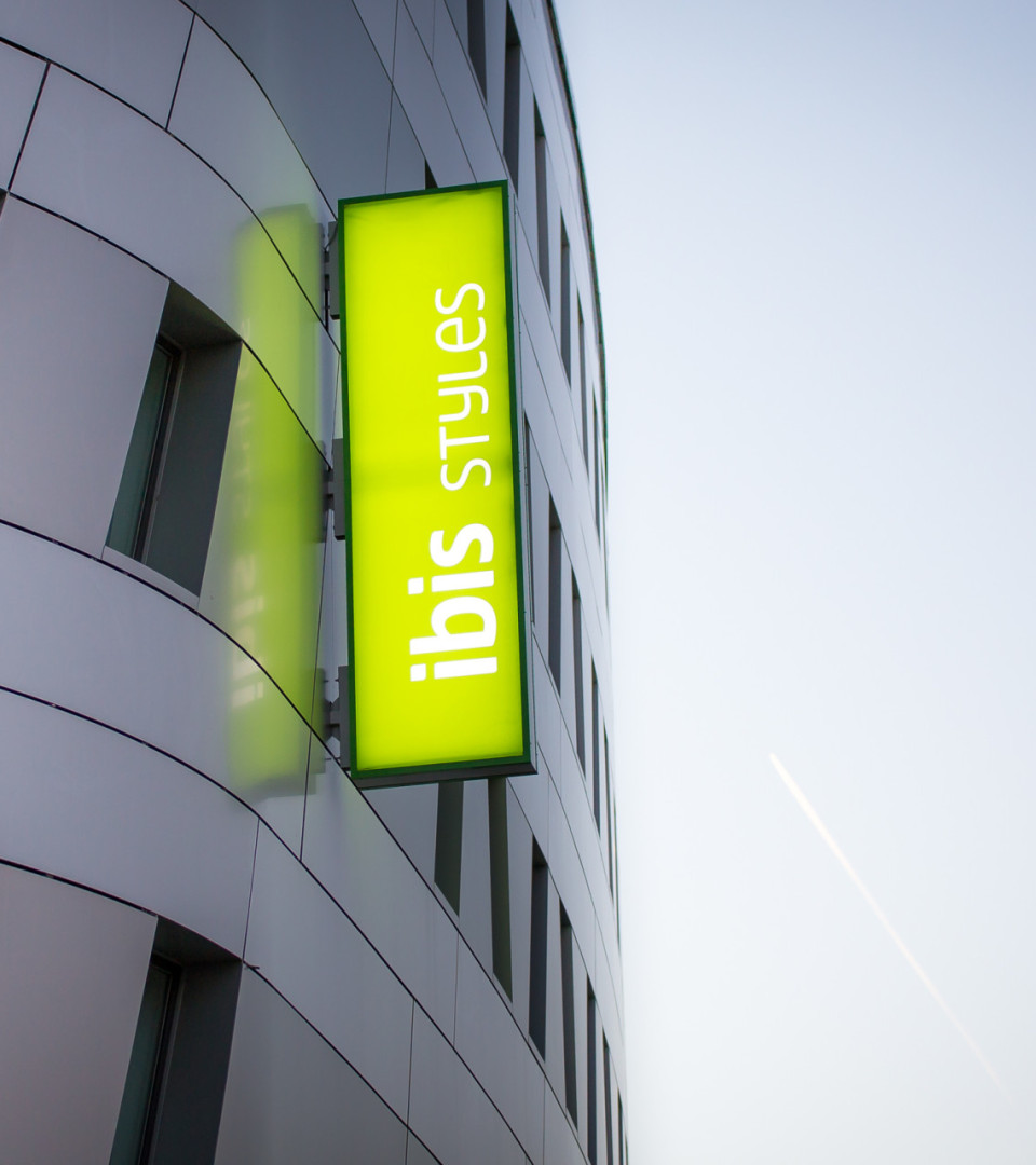 green lightbox sign displaying ibis styles on a modern building's wall